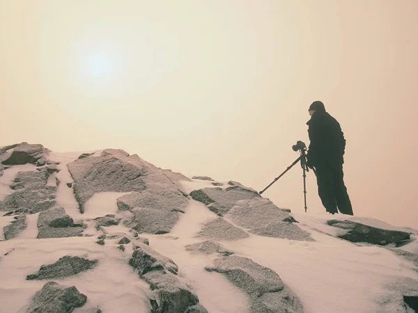 Fotógrafo de viajes haciendo fotos en piedras antiguas en el pico nevado de la montaña. Mañana de invierno — Foto de Stock