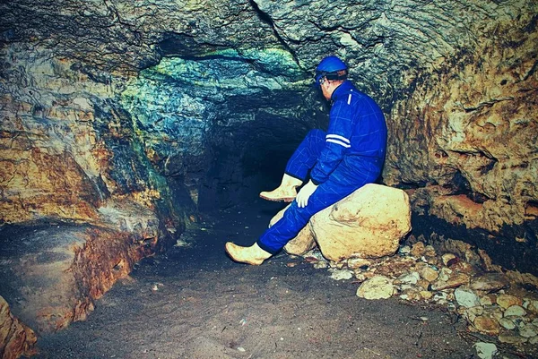 Site contractor engineer in blue overal, rubber boots and protective helmet in subterranean tunnel.