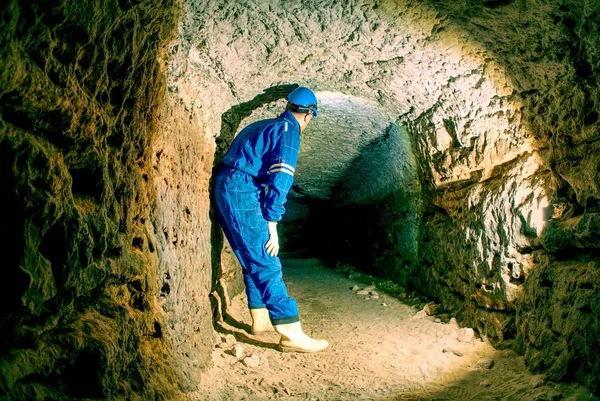 Obrero encorvado en azul en general y casco de seguridad en túnel subterráneo. Empleo peligroso . — Foto de Stock