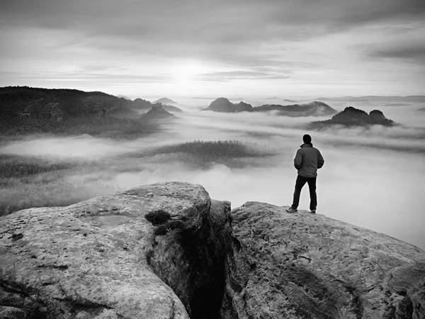 Wanderer auf dem felsigen Gipfel. herrlicher Tagesanbruch in den Bergen, dichter Nebel im tiefen Tal. . Schwarz-Weiß-Foto. — Stockfoto