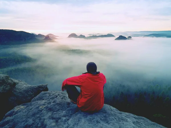 Visão traseira para o viajante ficar sozinho no penhasco com névoa abaixo pernas, luz do sol no céu nublado — Fotografia de Stock