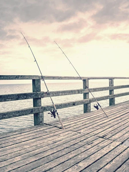 A fából készült korlát a beach pier ellen több horgászbot. — Stock Fotó