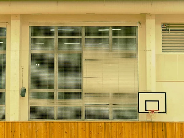 Interior del gimnasio de la escuela con tablero de baloncesto y cesta. Redes de seguridad sobre ventanas . —  Fotos de Stock