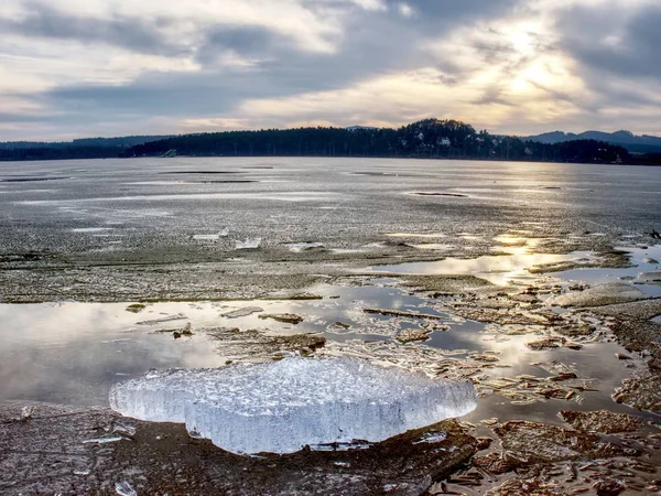 Exposed shore under melting ice. Close up view to border between ice and dark water. — Stock Photo, Image