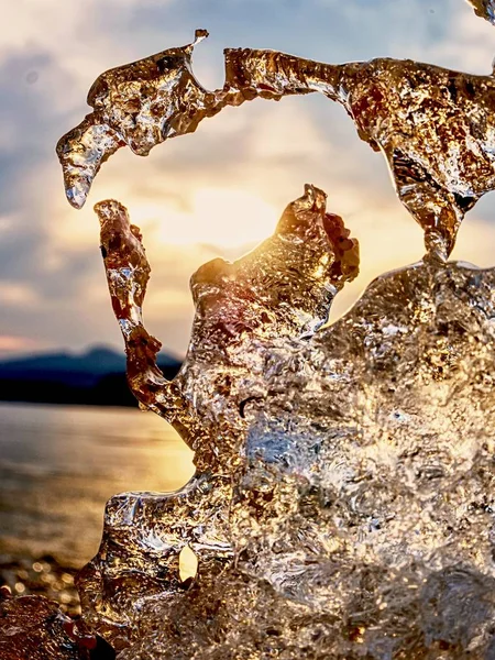 Parlak soğuk buz donmuş gölün kıyısında parlak buz sarkıtları. Gün batımının sıcak güneş ışınları. Yansıma — Stok fotoğraf