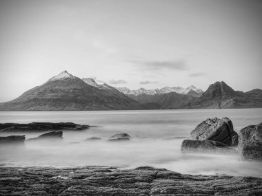 Peaceful dawn at Elgol bay. Low angle  overlooking of offshore rocks and smooth sea, mountains  clipart
