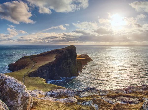 Neist Point lighthouse on rocky cliff above wavy sea. Blue evening sea and sharp cliffs,