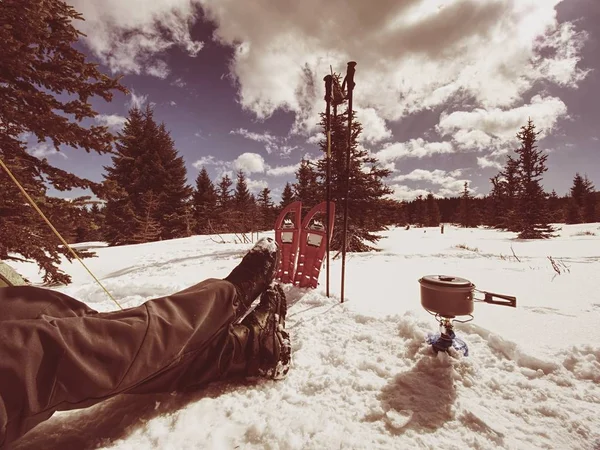 Almuerzo de cocina y el hombre descansando durante el sendero de invierno. raquetas de nieve y bastones — Foto de Stock