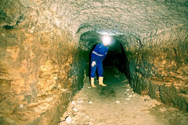 Man in underground tunnel works. Employee in safety suit works in medieval tunnel