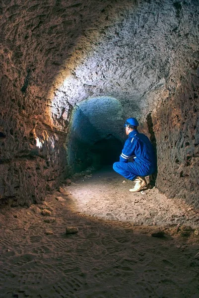 El hombre en túnel subterráneo trabaja. Empleado en traje de seguridad trabaja en túnel medieval — Foto de Stock