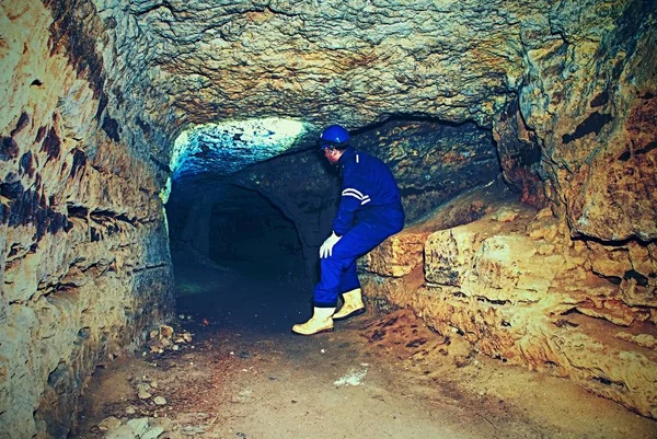 Obrero encorvado en azul en general y casco de seguridad en túnel subterráneo. Empleo peligroso . — Foto de Stock