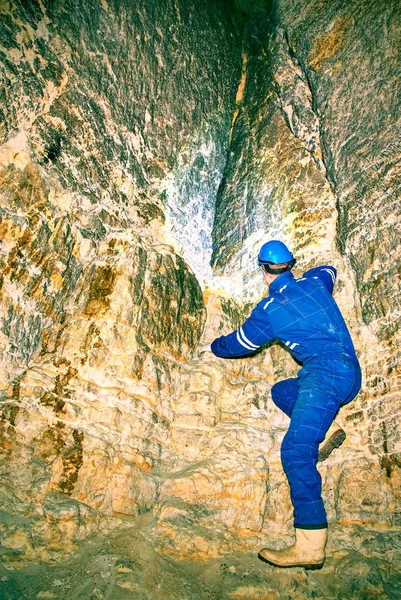 Hunched worker in blue overall and safety helmet in underground tunnel. Dangerous employment. — Stock Photo, Image