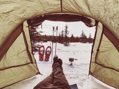 Yemek pişirme ve kış iz sırasında oturan adam. Kar ayakkabılarını ve direkleri