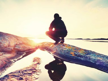 Kayalık bir göl kıyısındaki üzerinde oturan ve düşünme yalnız turist adam. Ücretsiz okyanus yukarıda güzel bir çok renkli batımında rahatlatıcı