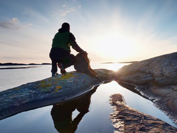 Jeune homme assis sur un rocher regardant un magnifique coucher de soleil sur la mer. Randonneur seul profiter de la soirée — Photo