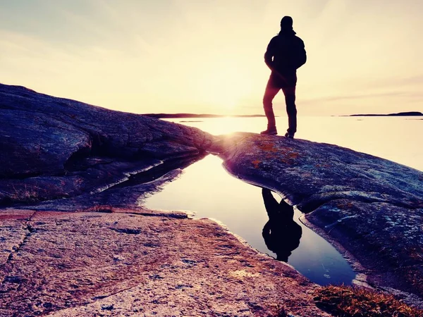 Silhouette d'homme en vêtements de plein air sur une falaise rocheuse au-dessus de la mer. Pensée de randonnée pendant le coucher du soleil — Photo
