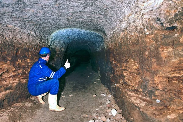 Man in underground tunnel works. Employee in safety suit works in medieval tunnel