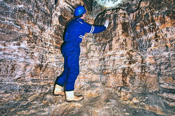 Site contractor engineer in blue overal, rubber boots and protective helmet in subterranean tunnel.