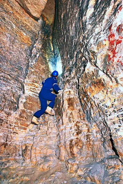 Site contractor engineer in blue overal, rubber boots and protective helmet in subterranean tunnel.