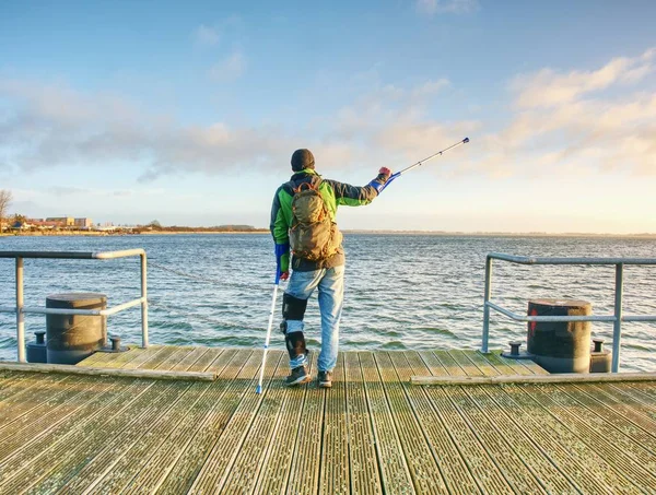 Un uomo con le stampelle al molo della talpa. Turista con gamba rotta sulle stampelle — Foto Stock