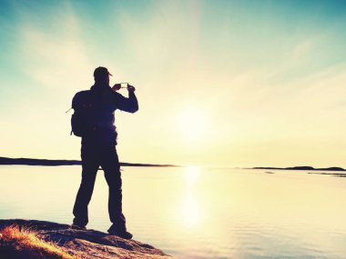 Deniz akşam gökyüzü karşı doğal görünümü karşı cep telefonunda selfie alarak yüksek turist. Güneş ayna