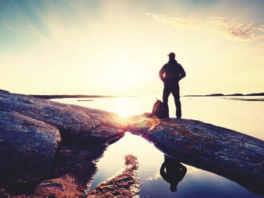 Kayanın üzerinde duran ve akşam güneşe doğru seyir adam silüeti. 