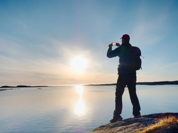 La silueta del hombre guarda recuerdos con el teléfono de la cámara en la mano. Maravillosa puesta de sol en el mar — Foto de Stock