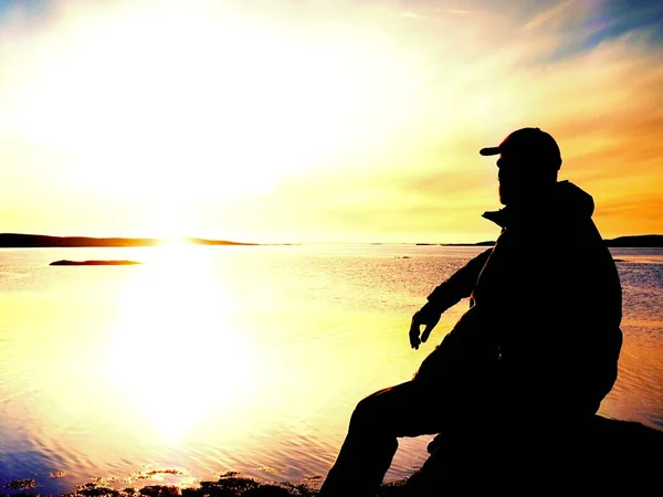 Junger Reisender bei Sonnenuntergang. Tourist sitzt auf der Klippe über dem See — Stockfoto