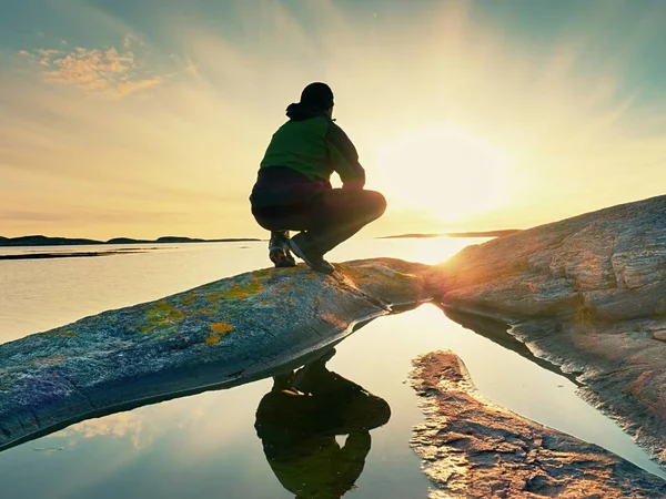 Jovem sentado numa rocha a ver um lindo pôr-do-sol no mar. Caminhante sozinho desfrutar da noite — Fotografia de Stock