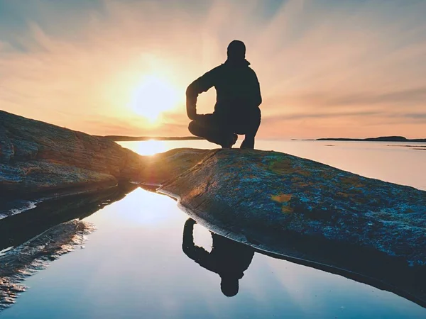 Caminhante solitário homem senta-se sozinho na costa e desfrutar do pôr do sol. Vista sobre penhasco rochoso para o oceano — Fotografia de Stock