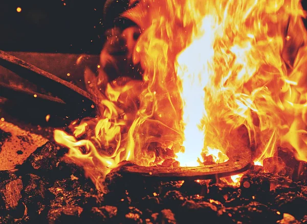 Fuego ardiente en la forja de carbón herrero. Metal rojo de forja en caliente — Foto de Stock