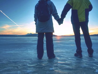 Aşıklar donmuş lagünde buzun üzerinde durup güneşi izliyorlar.