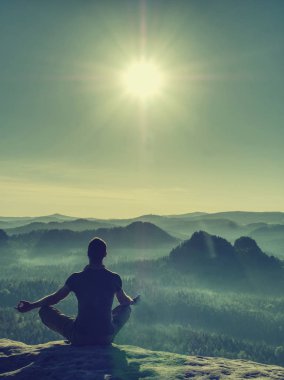 Kovboy şapkası takan yalnız bir adam büyük bir kayanın üzerinde oturuyor. 