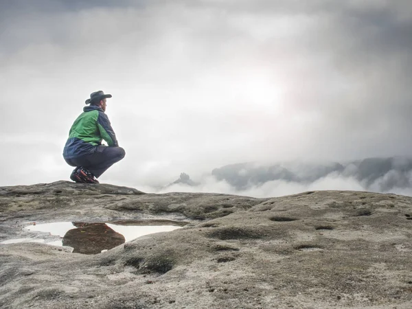 Homem solitário se senta no penhasco apreciar a vista sobre o vale cheio de névoa — Fotografia de Stock