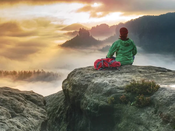 Alone girl sits with her back on cliff against huge misty mountain — 스톡 사진