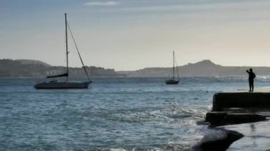 Orta arazideki düz çimento iskelede aktif orta yaşlı kadın gezgin öğlen güneşine karşı yatları demirlemiş. İspanya Mallorka adasında Ocak ayı içinde dalgalı deniz.