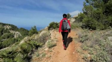Mallorka Adası 'nda dağ yürüyüşü yapan bir kadın. Sıcak ve güneşli bir bahar günü. Rocky kumlu patika, çam ağaçları, çalılar ve palmiyeler.