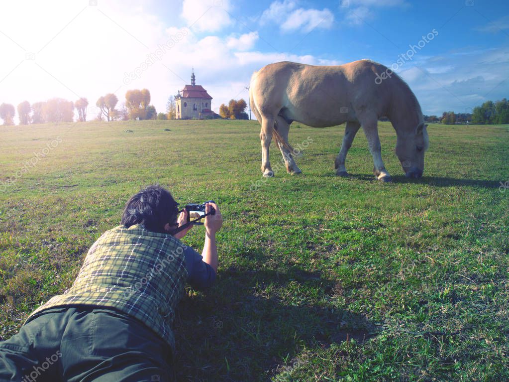 Photographer lying down on grass and photographing horse