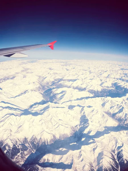 Крыло самолета над снегом покрыло острые зимние горы — стоковое фото