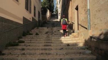 Sırt çantalı şapkalı gezgin kız eski kasaba sokağından geçiyor. Öğrenci seyahati kavramı. Sırt çantalı kız tarihi kaleye doğru adım adım yürüyor 