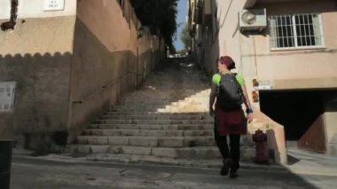 Tarihi eski kasabadaki taşlı merdivenlerde yükselen bir kadın. Sırt çantalı kız tarihi kaleye doğru adım adım yürüyor 