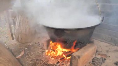 Eldivenli aşçı domuz eti ve kemiklerle kazanın kapağını açar. Kamp ateşinde tencerede yemek pişirmek..