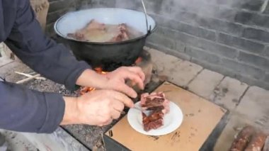 Çatal ve tabakla aşçı, pişmiş pirzolaları buharlı bir tencereden çıkarır. Açık ateşte parti için geleneksel şarküteri pişirme.