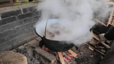 Yangının üstünde domuz pirzolası pişirmek. Buhar ve koku kapağın altından çıkıyor. Adam odunları şömineye koyar..