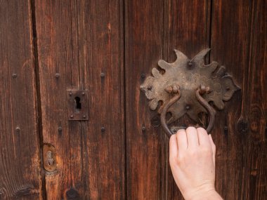 Eski ahşap kapısında siyah demir tokmaklı kadın eli. El kapıyı tıklatıyor. Yaklaş, seçici odaklanma