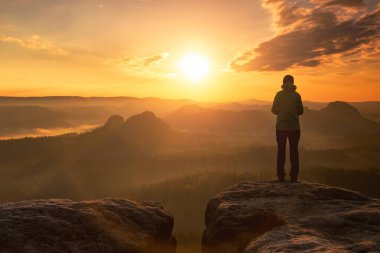 Şapkalı ve yeşil ceketli hippi bir genç kız. İnanılmaz bir manzarada yeni bir günün doğuşunu seyrediyor. Sisli dağ modelinin keskin zirvesi. Gezgin turist arka planda güneş ışığı yolculuğunda 
