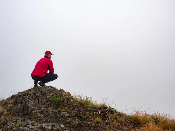 Red man sits on the edge of a cliff and looks at the invisible valley  in heavy mist. Strange weather