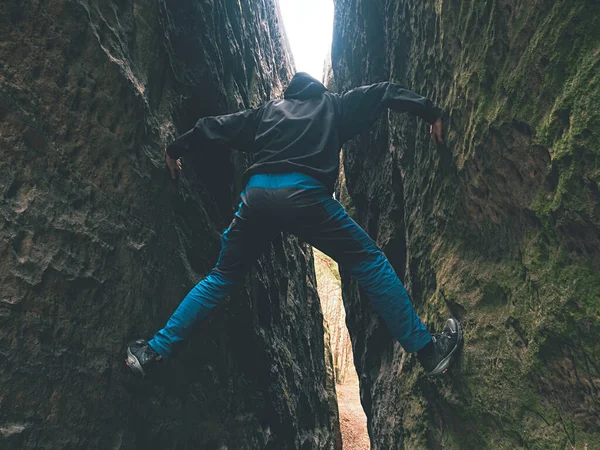 面白い男岩壁の間に登る 男は青いズボンと黒のジャケットを着用 — ストック写真