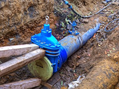 Yeraltındaki 300mm 'lik su borusunda yeni bir mavi kelebek vanası. Çelik ve Beden Eğitimi boru hattı kazıda yolun altında