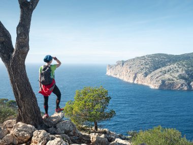 Girl traveler overwatching the bay at Es Camp de Mar town, Mallorca.  Mountain  trail along west shore. clipart